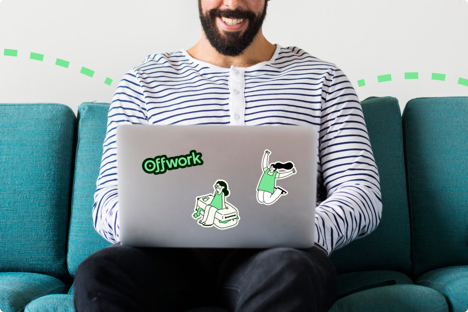 A man sitting on a couch with a laptop covered in Offwork stickers